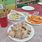 Na czerwonym obrusie stoją talerze z ciasteczkami w kształcie gwiazdek, paluszkami marchewkowymi, rolkami waflowymi i paluszkami precelkowymi.