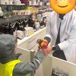 Dziecko w odblaskowej kamizelce wręcza mały bukiet kolorowych kwiatów farmaceutce w aptece.