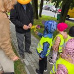 Dziecko w kamizelce wręcza kwiaty seniorowi.