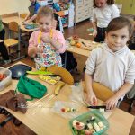 Dzieci w klasie szkolnej przygotowują owocowe przekąski i szaszłyki przy stolikach.